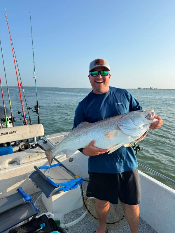 Smiling angler in sunglasses holding a large redfish on a boat with fishing rods in background
