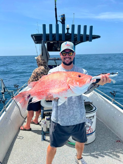 Smiling angler in sunglasses holding a large red snapper on a fishing charter boat