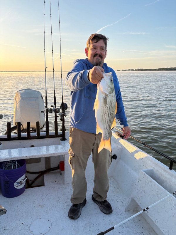 Smiling man holding a striped bass on a fishing boat at sunset