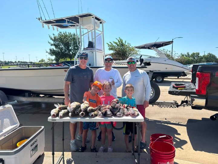 Three men and three kids posing with a big catch of fish on a table at the marina