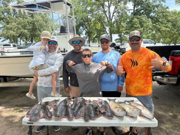 Group of six anglers, including a child, posing with a fresh catfish catch on a fishing charter