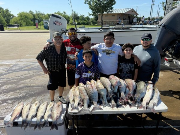 Group of seven anglers posing with a large catch of striped bass on tables at the dock
