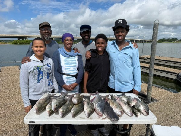 Family of six standing on a dock smiling with a table full of freshly caught fish