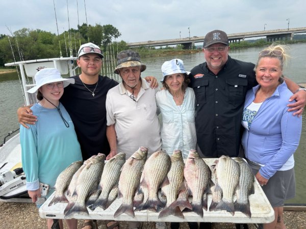 Family of six posing with a striped bass catch on a dock during a guided fishing charter