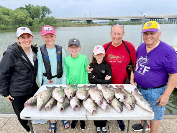 Family of six smiling behind a table full of freshly caught striped bass by the river