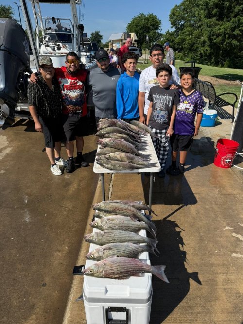 Group of family members posing with a striped bass catch on a dock beside a table and cooler