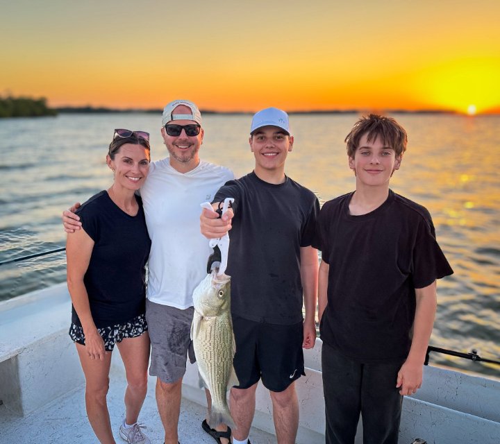 Family of four smiling on a boat at sunset, holding a freshly caught fish