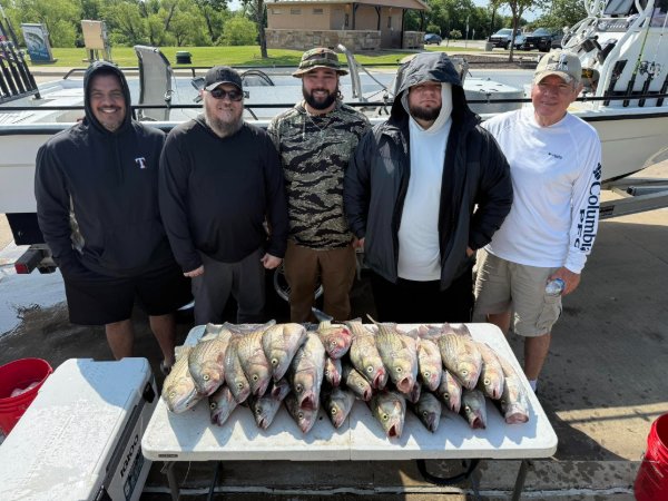 Five men standing behind a table displaying their fresh catch of fish after a fishing trip