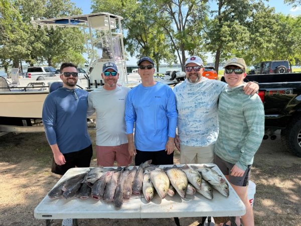 Five smiling men standing behind a table of fresh caught fish at a lakeside fishing trip