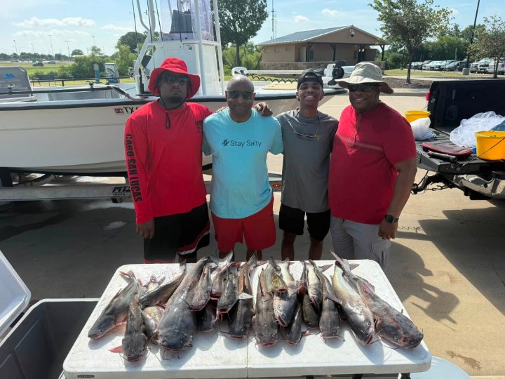 Four smiling anglers standing behind a table of freshly caught catfish at the dock