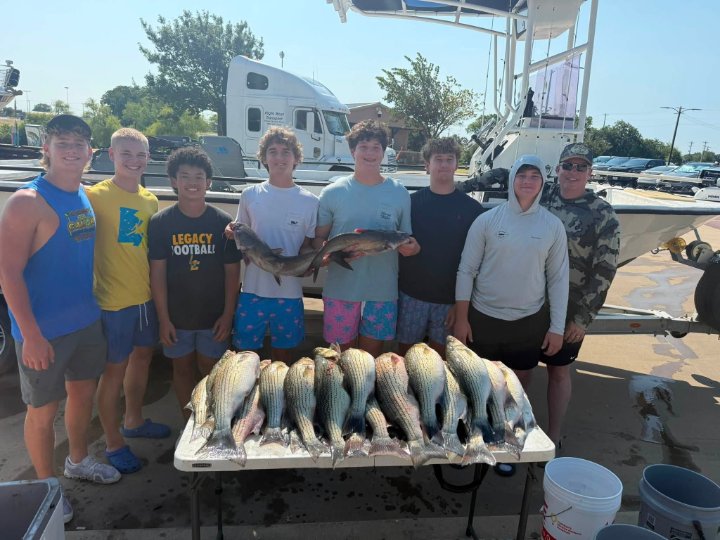 Group of young anglers and guide posing with striped bass and catfish catch on charter boat
