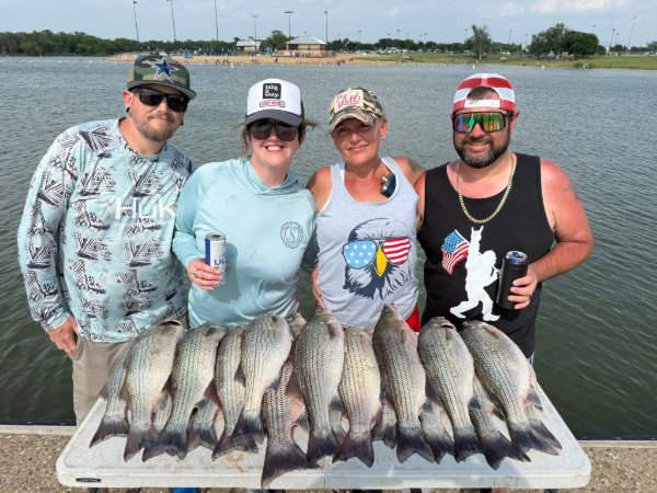 Four smiling anglers holding drinks pose behind a table of freshly caught white bass at the lake