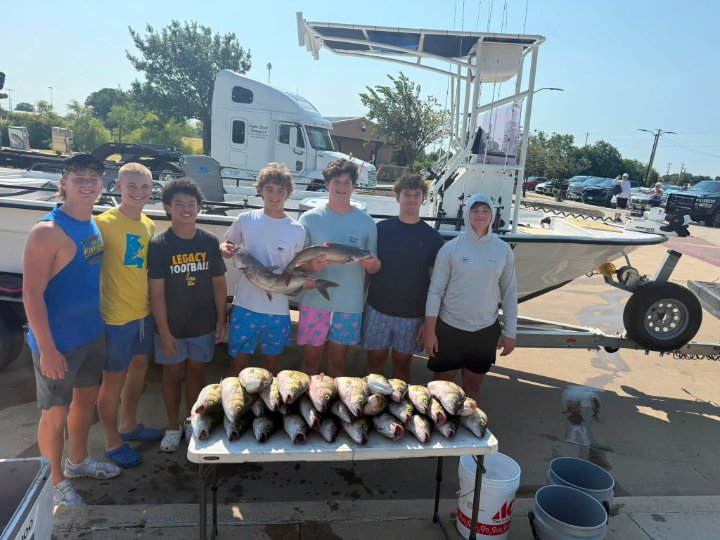 Seven teenage boys posing with a large catch of fish on a table beside a charter fishing boat