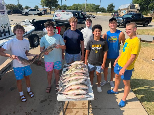 Group of teenage boys posing with a table full of fresh catfish catch from a fishing trip