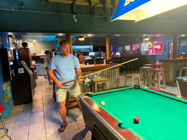 Man in blue shirt holding pool cue preparing to shoot at a bar pool table