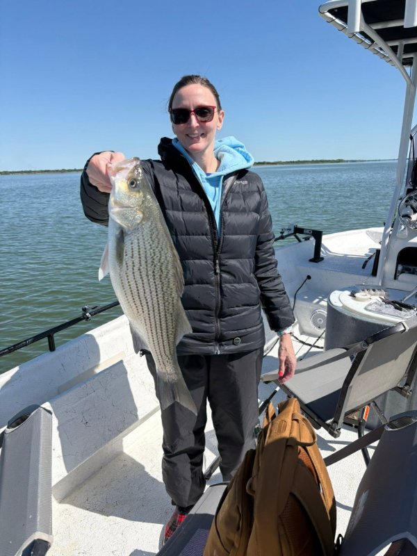 Smiling woman in sunglasses holding a striped bass catch on a boat under clear skies